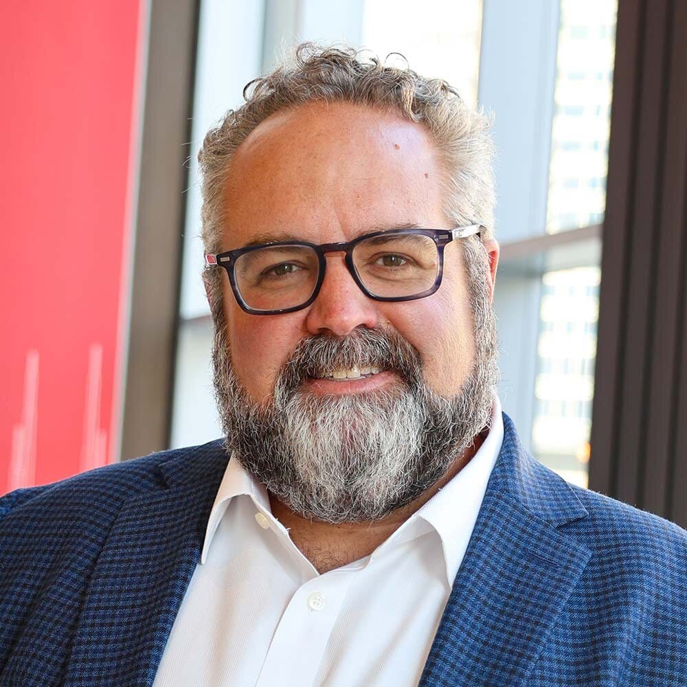 Caucasian man with beard and glasses wearing a blue jacket