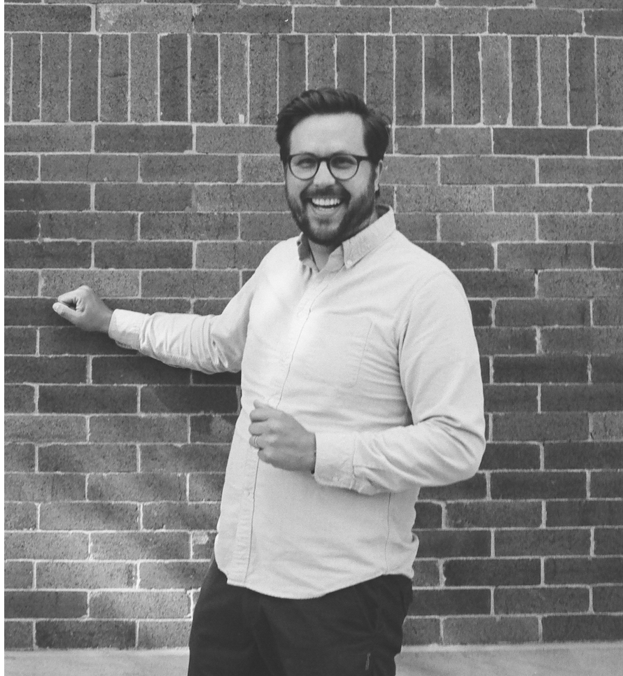 A black and white image of a man with glasses and button up shirt.
