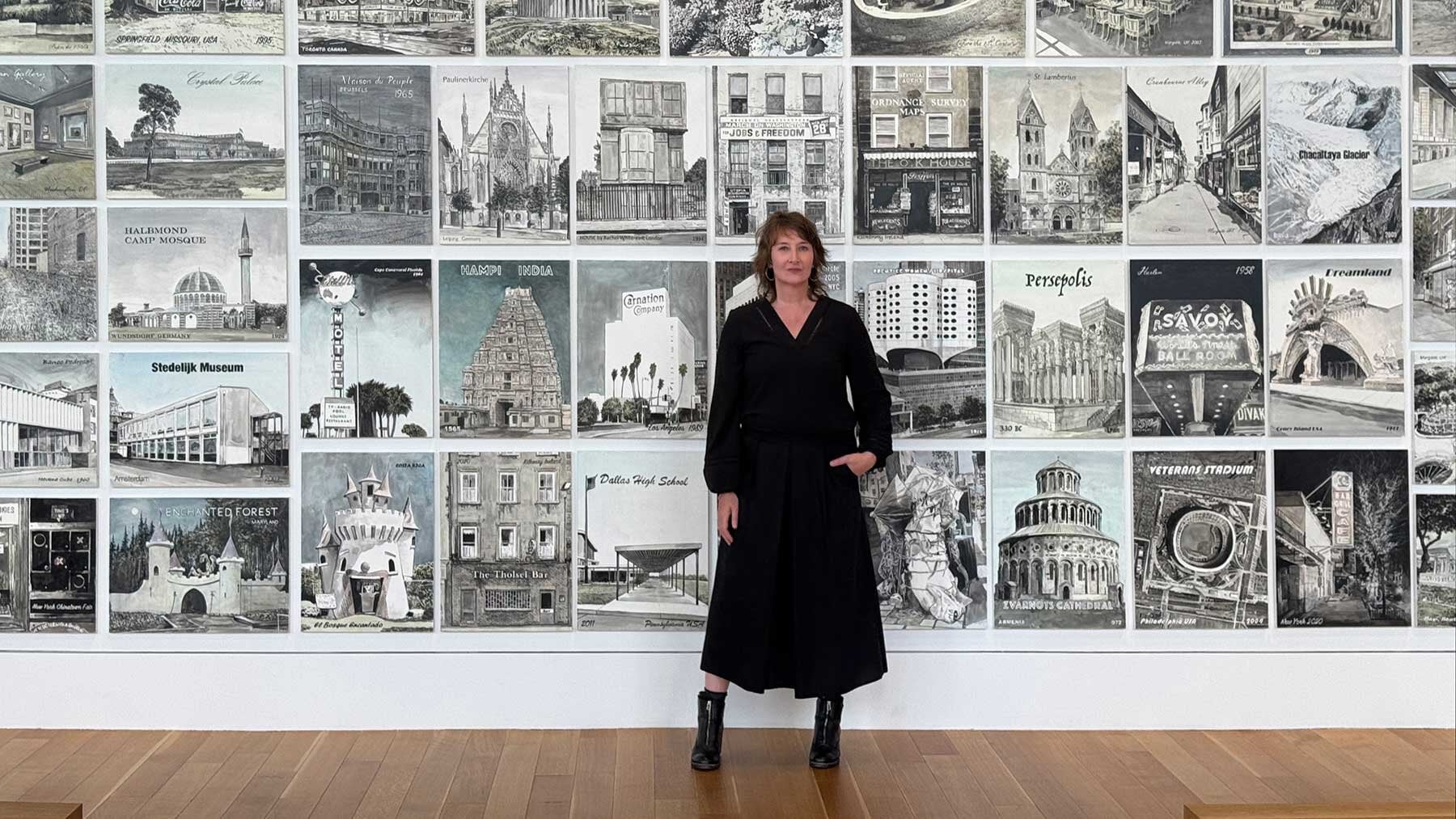 Lady in black dress standing in front of a wall of black and white paintings