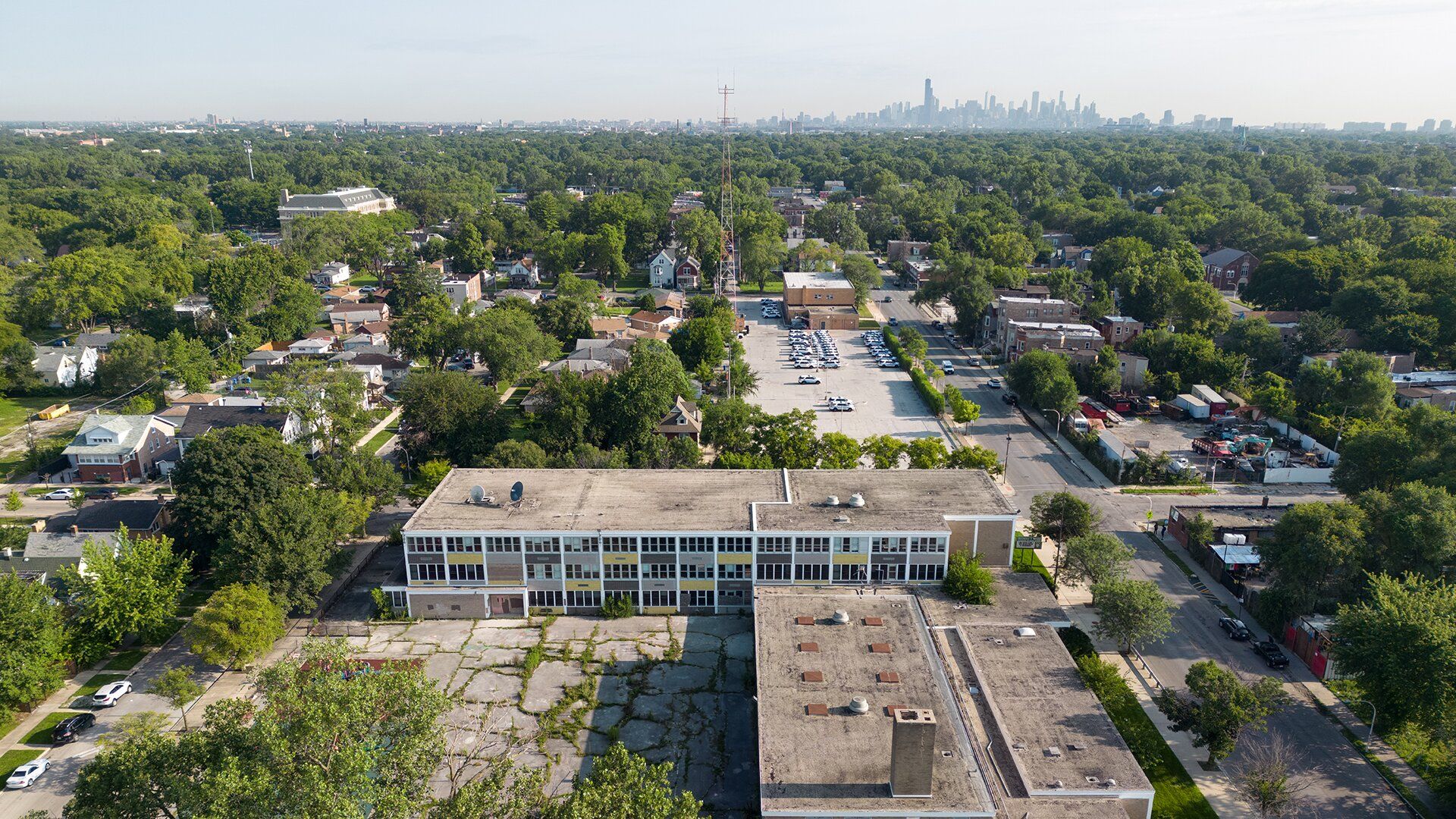 Aerial image of an abandoned rectangular building surrounded by trees and other smaller buildings. 