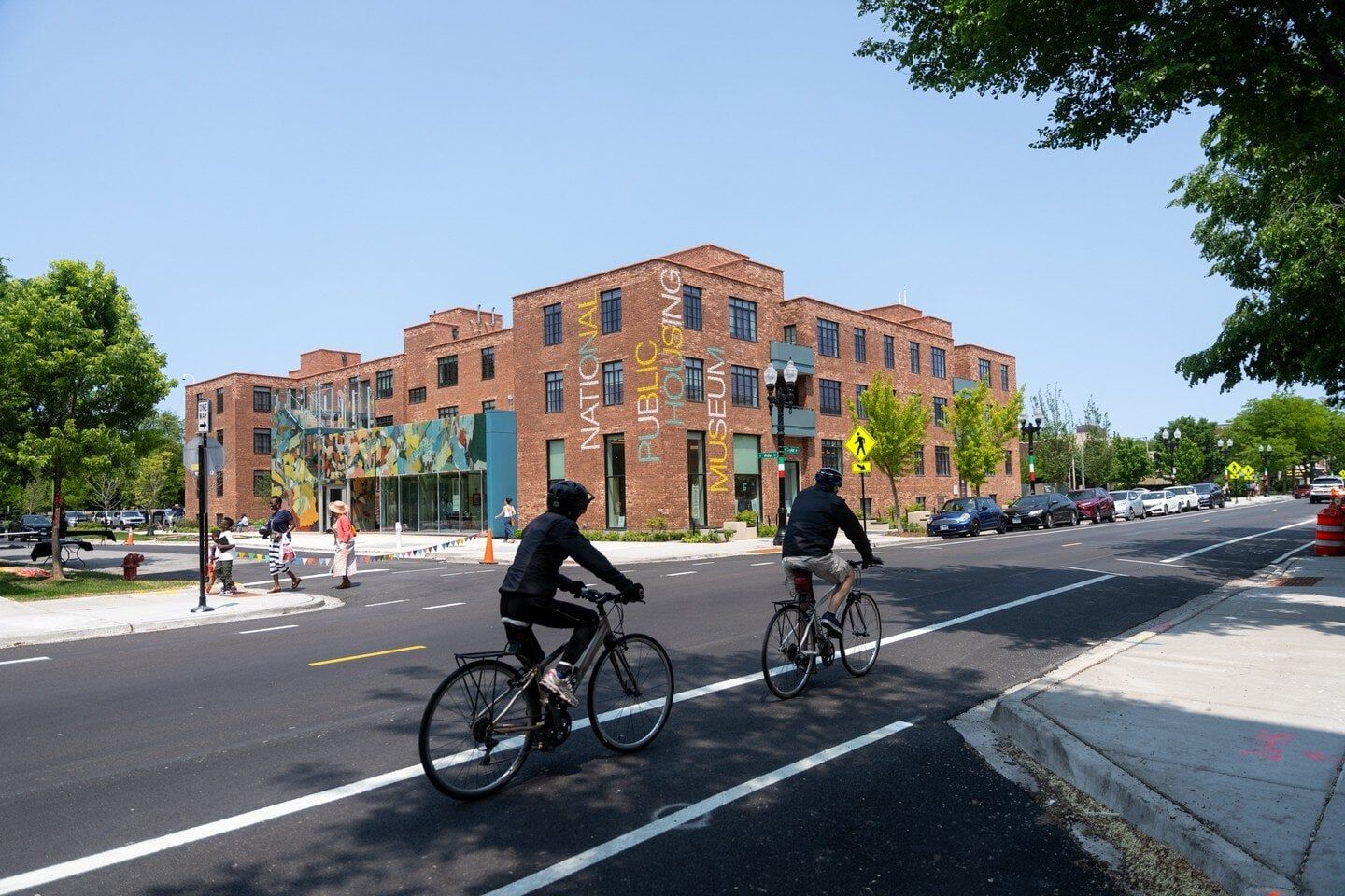 Two bicyclists riding in the city with a brick building in the foreground