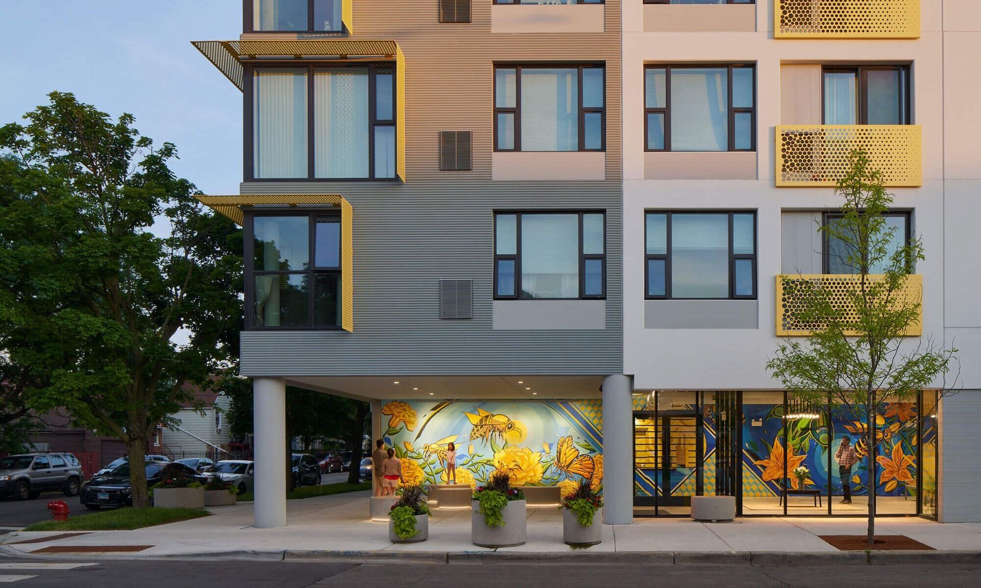 Image of a multi story building with the top out of frame. There is a mural of bees on the first floor and yellow metal sheets added as decoration.