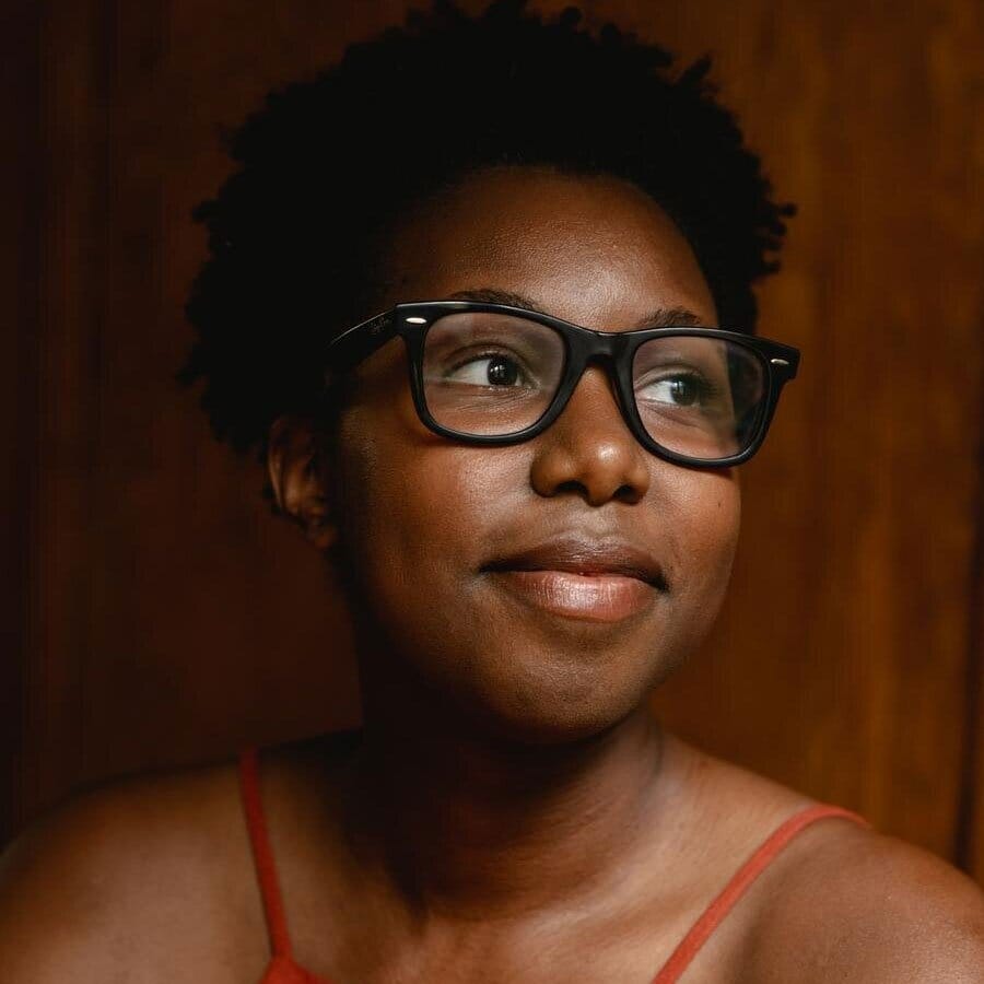headshot of a young black woman smiling and looking away with black framed glasses