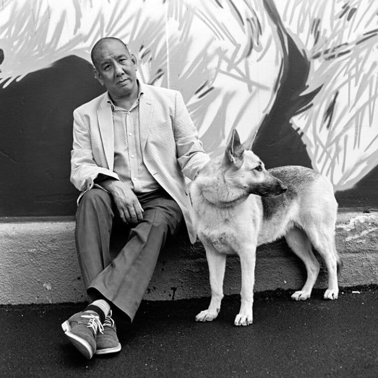 Headshot of a caucasian man with a beard in a black suit jacket standing against a wall
