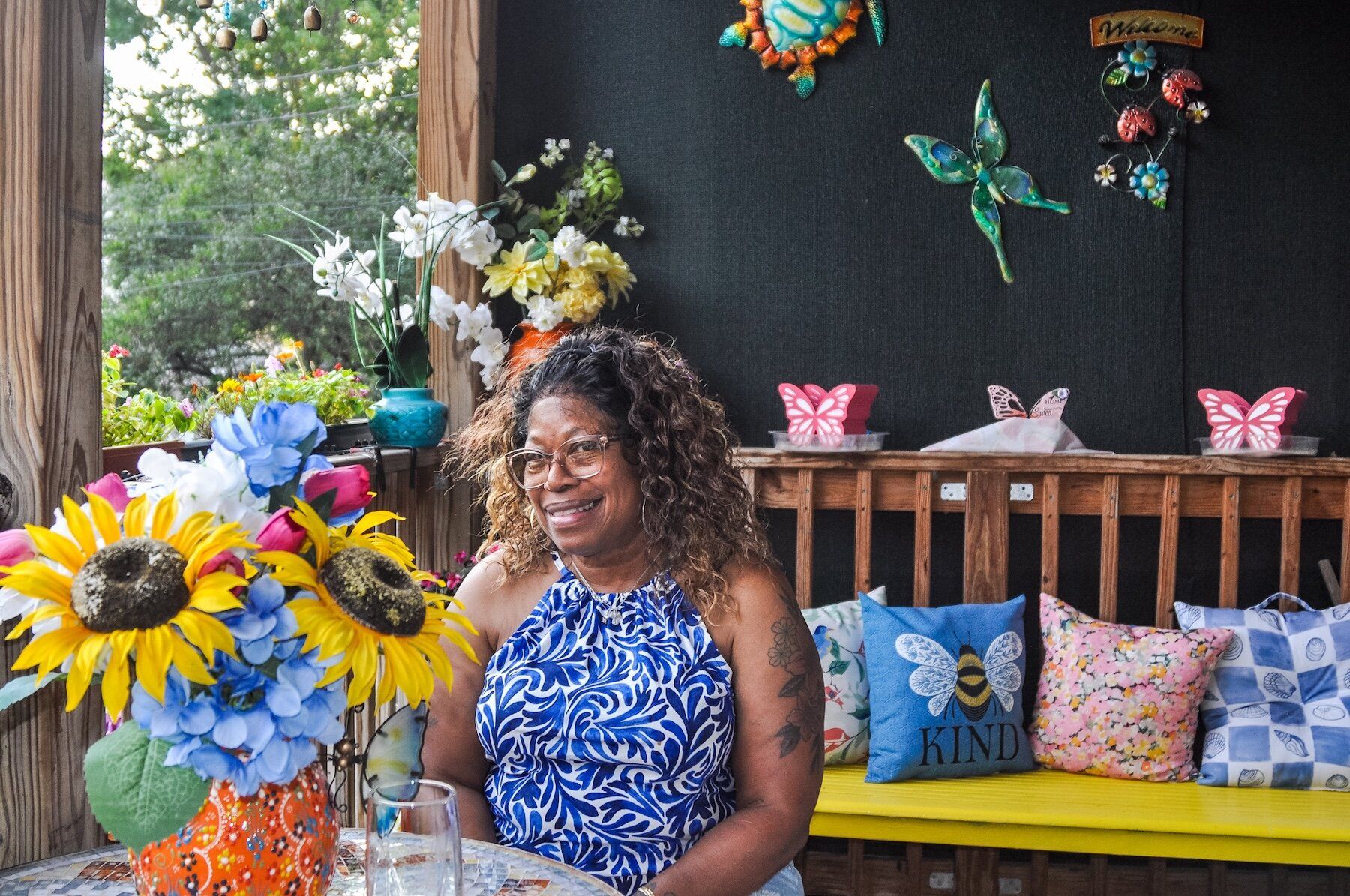 Woman in a blue shirt smiling next to some flowers.