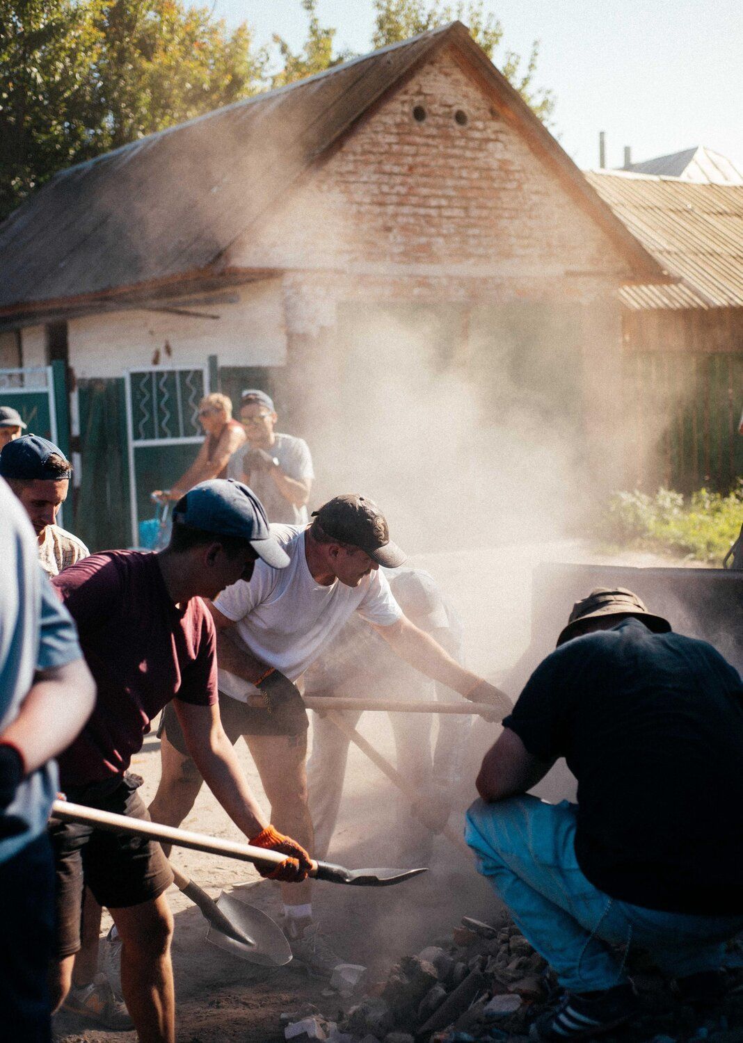 Men with shovels digging outside in a smokey area with a building in the background. 