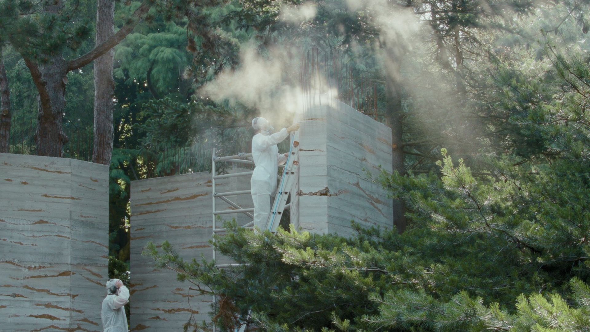 Outdoor with greenery surround, two men in white are work on a large wall