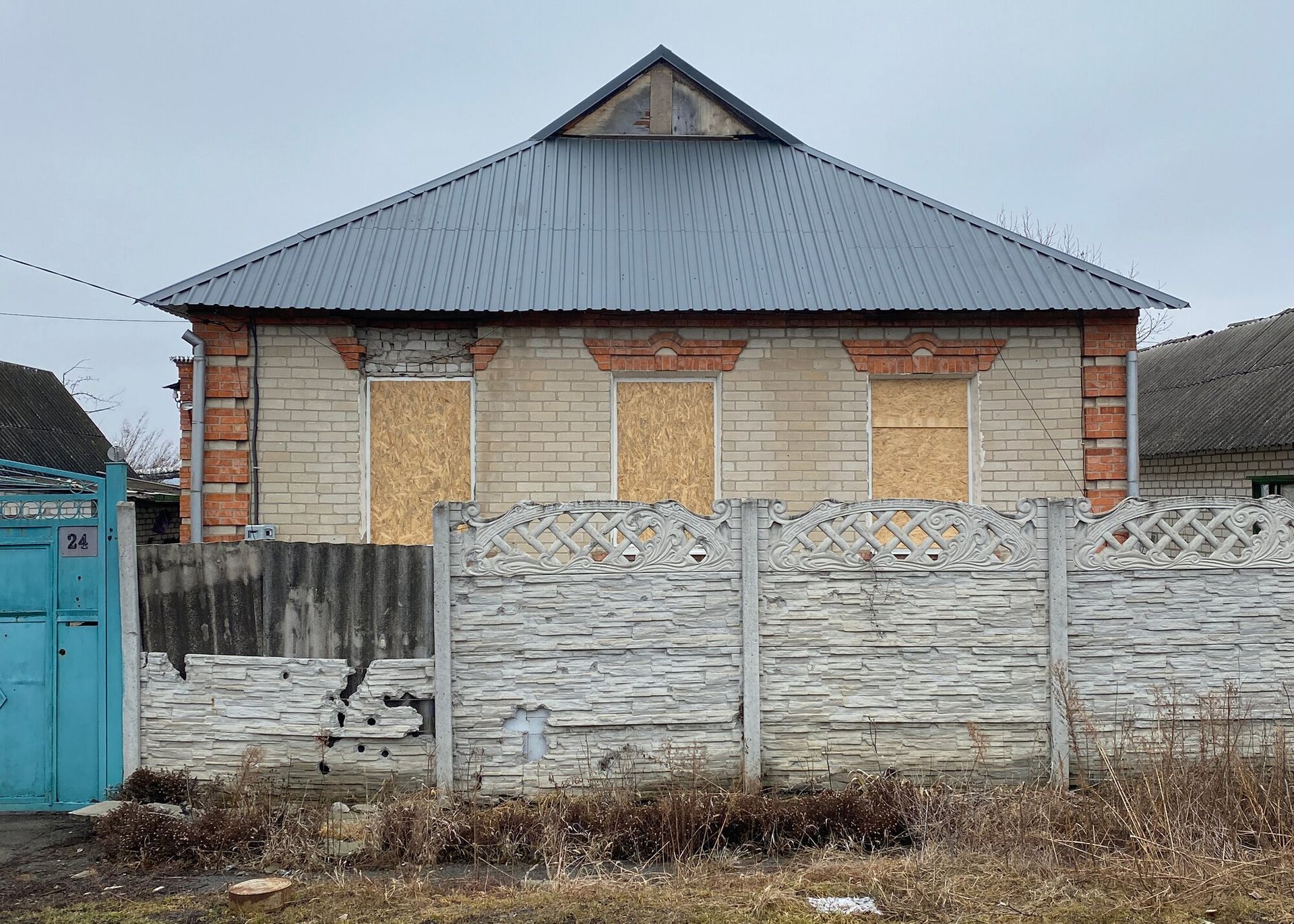 Image of a brick building with a metal roof behind a wood fence.