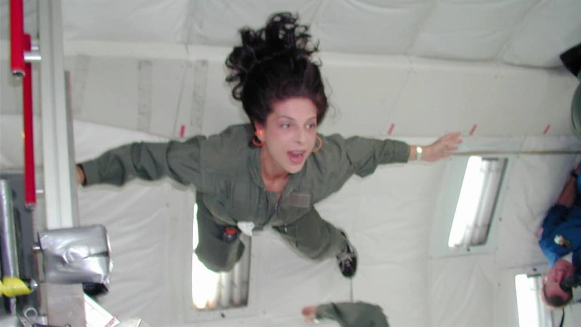 A woman floating in a gravity defying stance with arms wide open looking at something off screen intently