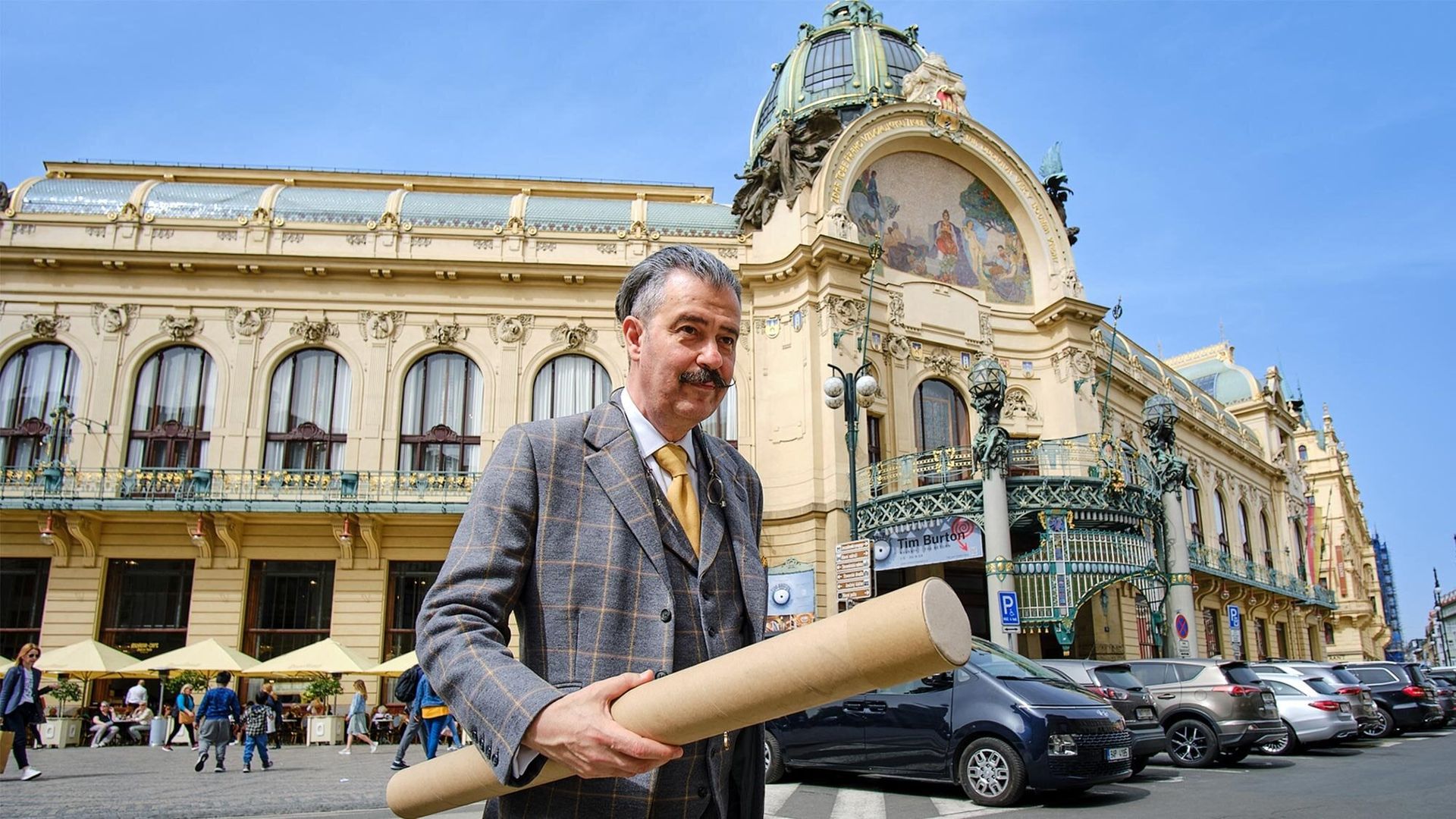 A man in a suit with a gold tie standing in front of an ornate old building