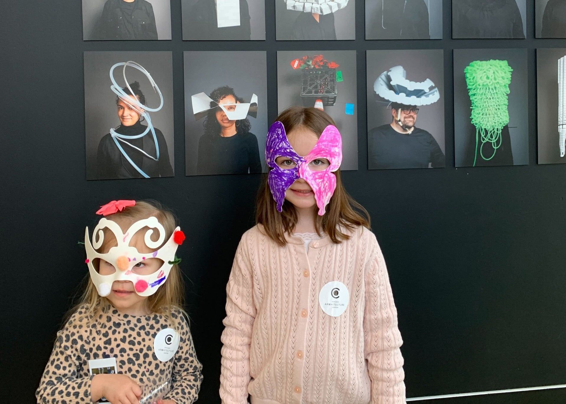 Two young girls with handmade face masks in front of a gallery of images