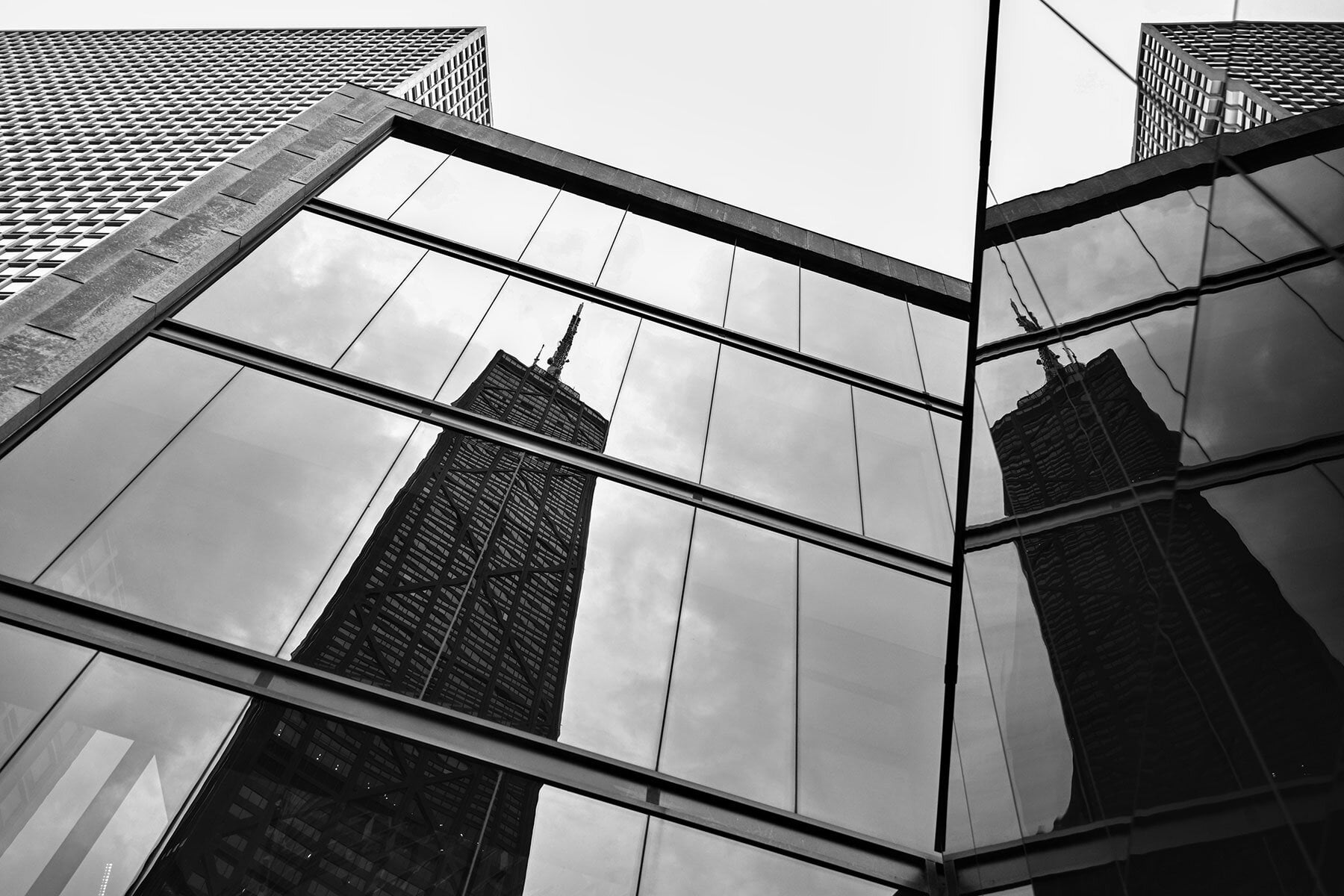 Black and white photo of a skyscraper with mirrored windows reflecting another skyscraper.