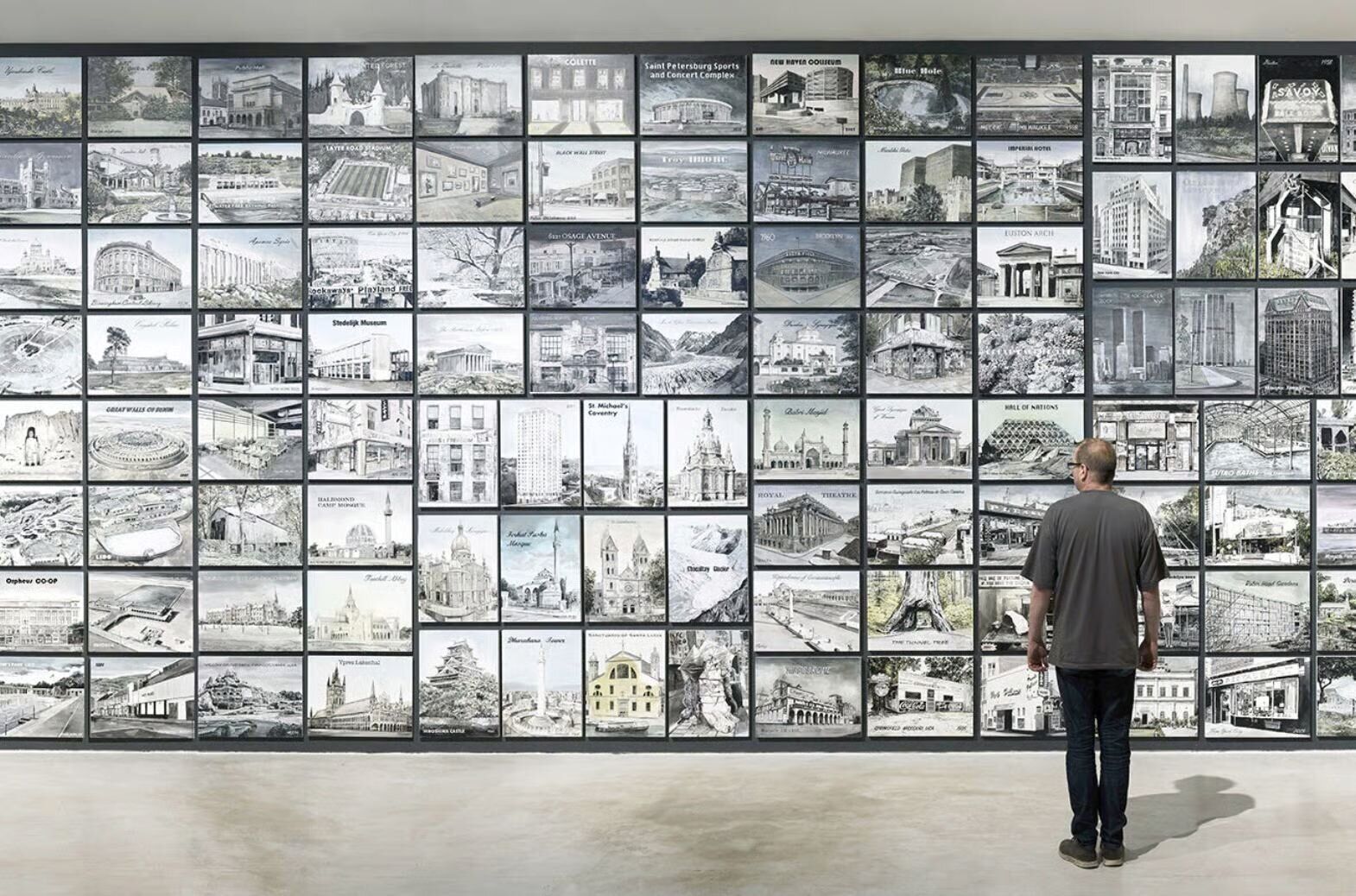 A man looking at a wall full of different images.