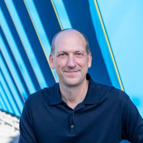 Image of a caucasian male in a dark polo smiling and looking straight