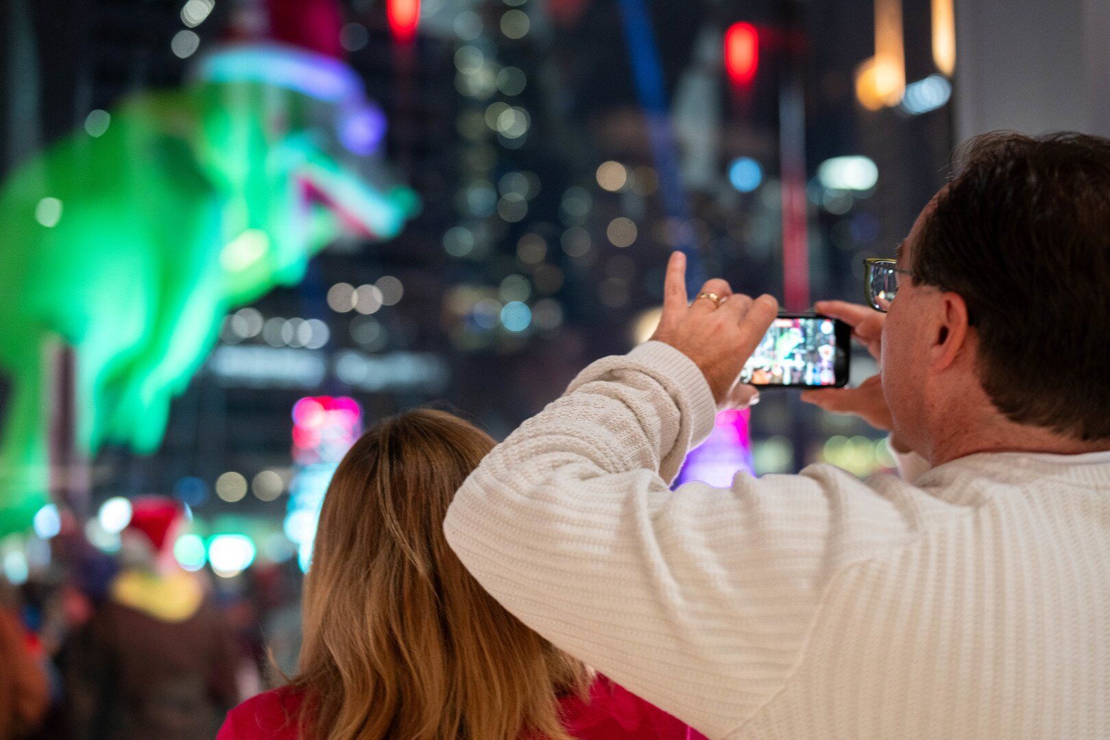 Man facing away taking a photo with his phone in the foreground, out of focus parade float in the background. 