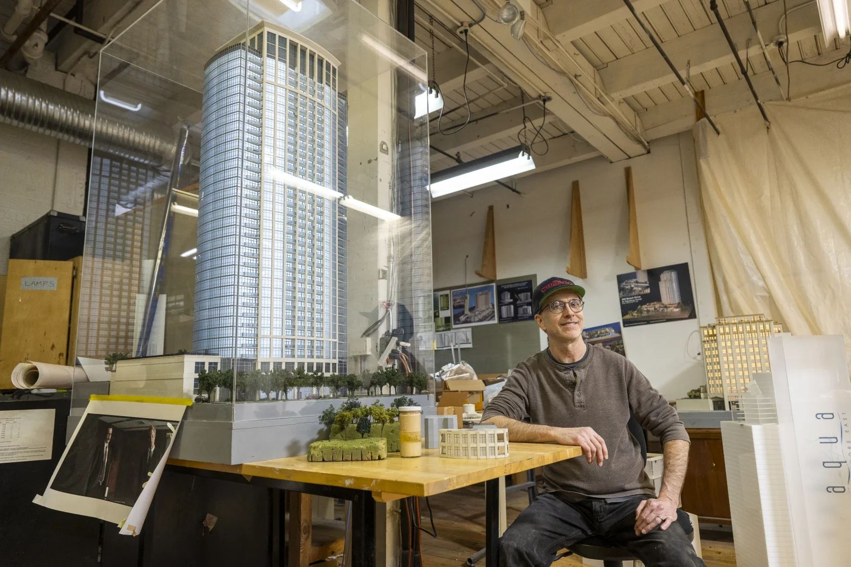 Caucasian man with a baseball cap seated in front of a skyscraper model inside.