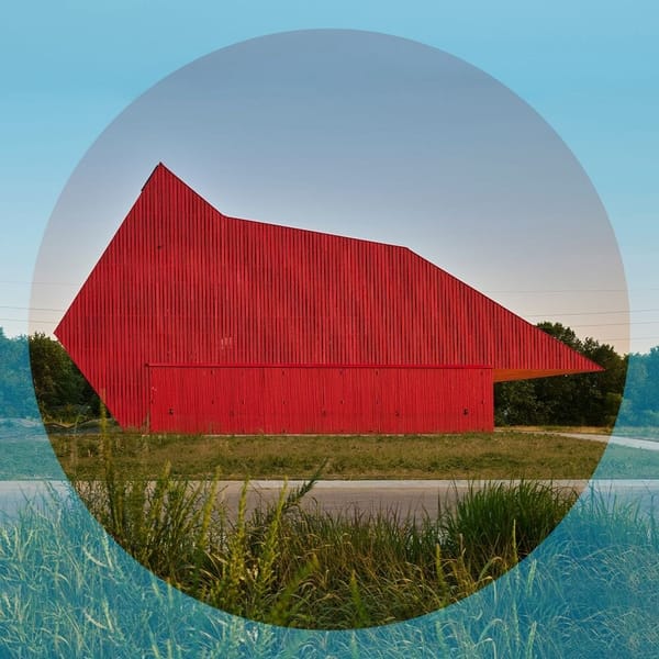 Large red angular building in the middle of a grassy field at dusk.
