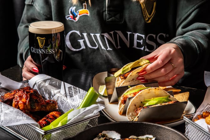 Someone holding tacos with a beer.
