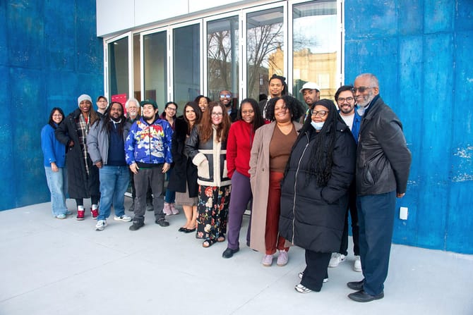 A group of diverse smiling people standing outside a building with a blue wall