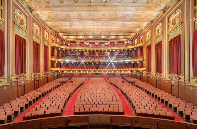 huge theater with red carpet, bright lights, and red seats.