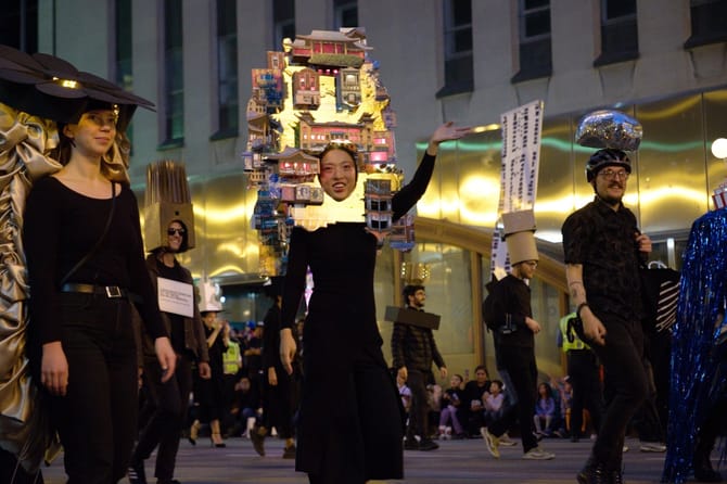 Image of a woman wearing all black and a tall headpiece waving.