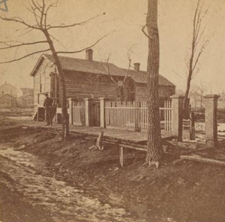 Old sepia tone image of a home with a picket fence.