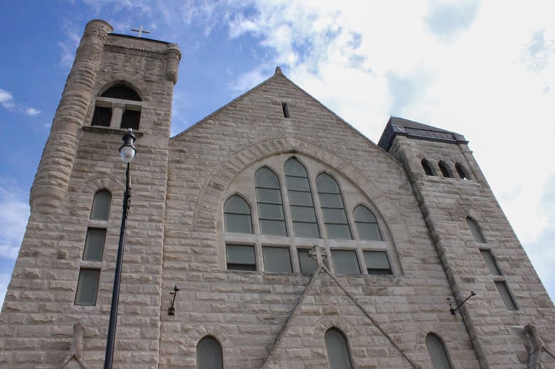 Looking up at a large church with a tan stone exterior and stain glass windows. 