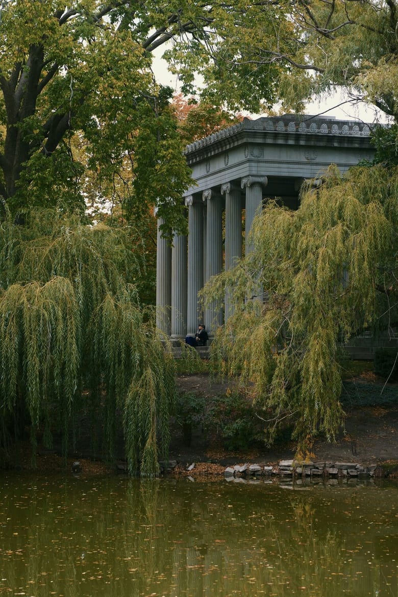 A lake in the foreground surrounded with greenery and a large structure with columns in the background. 