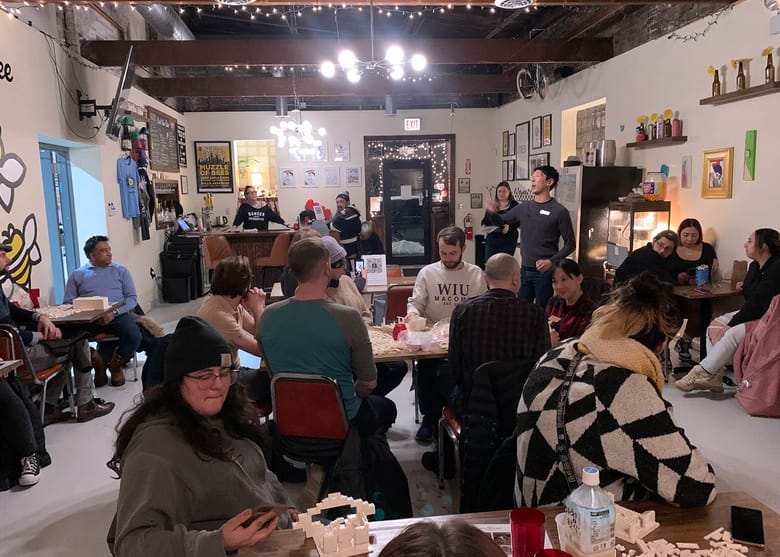 Inside a cider shop with tables with people and legos with a male facilitator speaking.