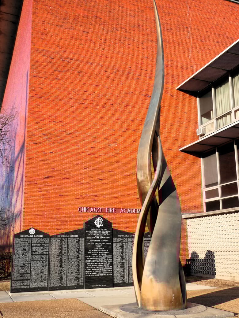 Bronze sculptural statue in front of brick wall.