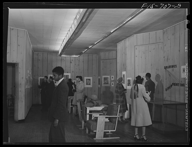 Black and white, interior of an exhibitions gallery with people looking at exhibits