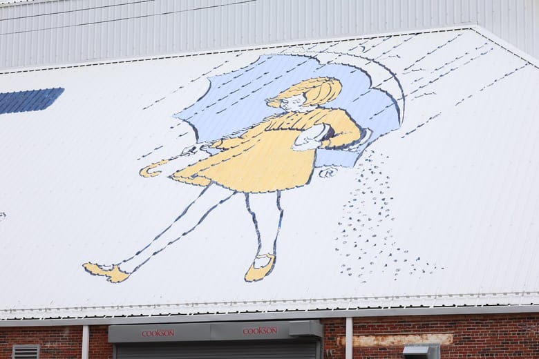 Illustration of a girl with a yellow dress and blue umbrella, painted on a roof.