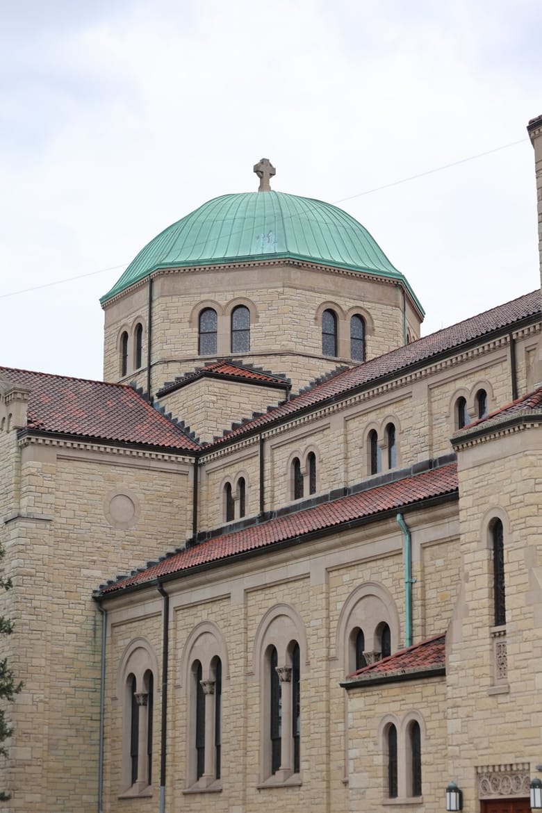Exterior of a cream and red brick church with a teal domed roof.
