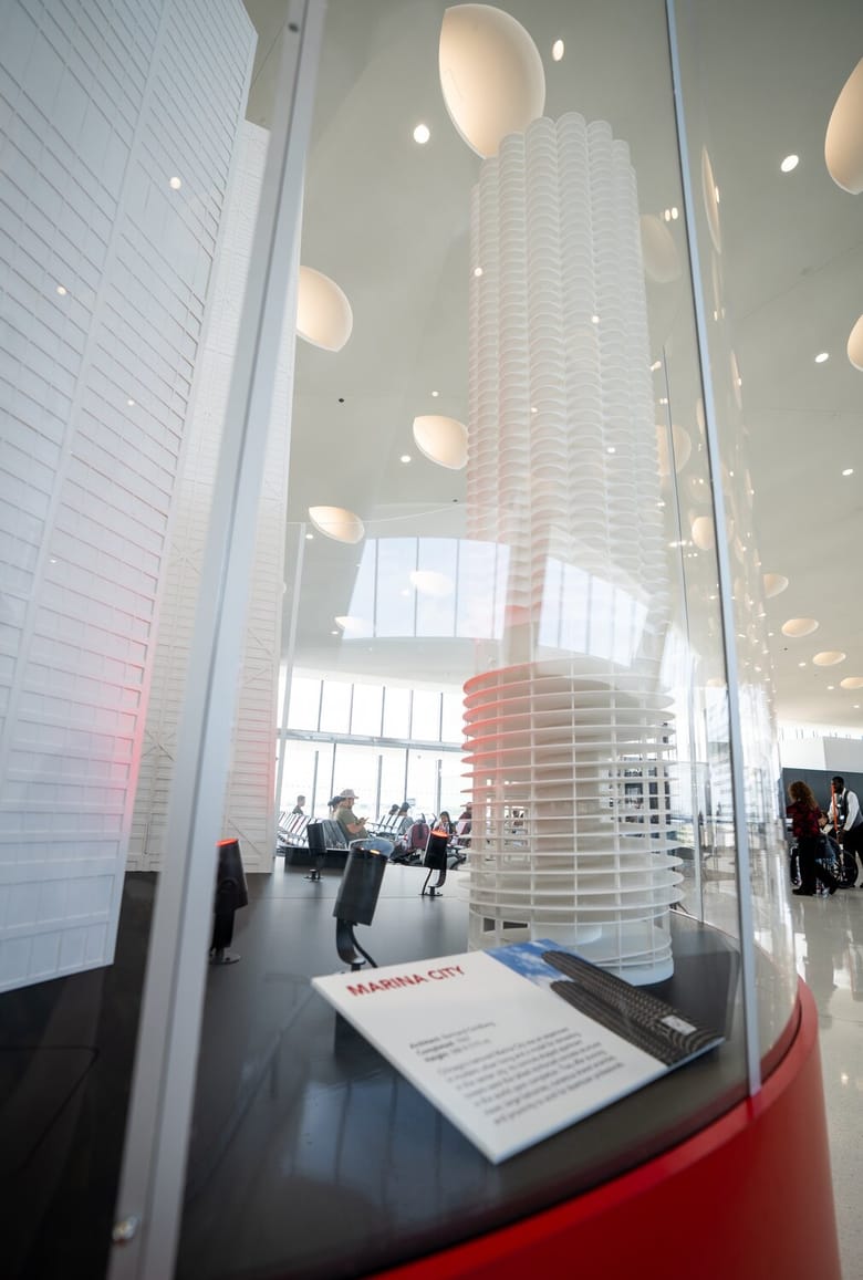 An exhibit with a red base and 3 white skyscrapers on it, in the middle of an airport.