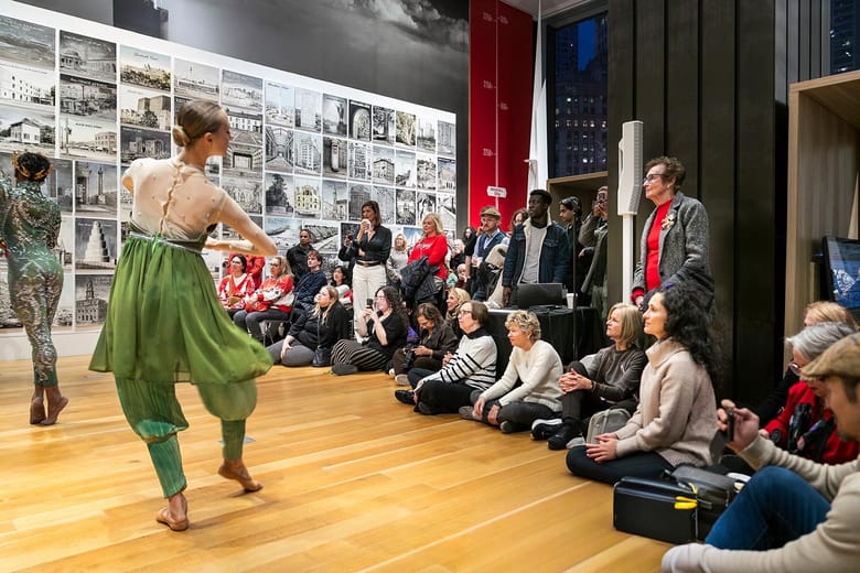 Dancers mid performance inside a gallery space while people look on.