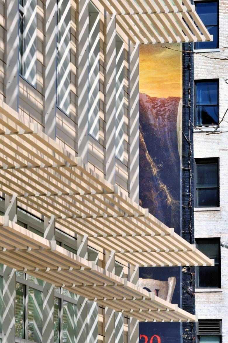 Tall building with overhanging beams casting striped shadows. 