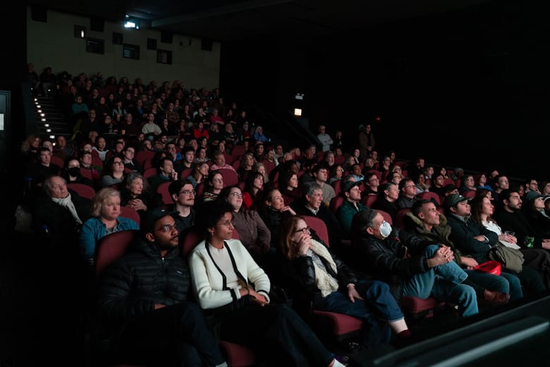 Image of a group of people sitting in a theater looking at a screen that is out of frame. 