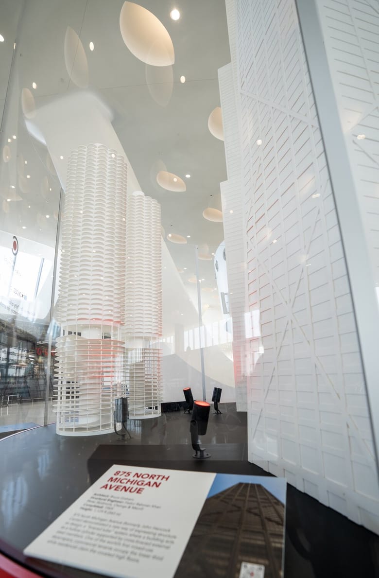An exhibit with a red base and 3 white skyscrapers on it, in the middle of an airport.