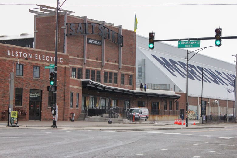 Image of a brick building in front of a large gray metal building with a slanted roof and "Morton Salt" painted on the side. 