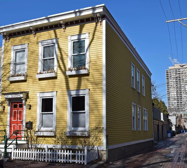 Yellow wooden house with white trim and window boxes filled with flowers. 
