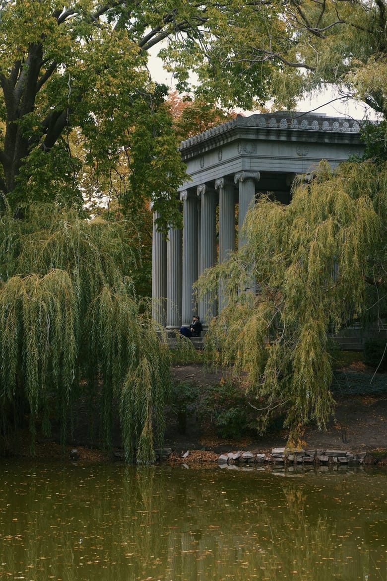 A mossy green pond with trees surrounding a building with pillars. 