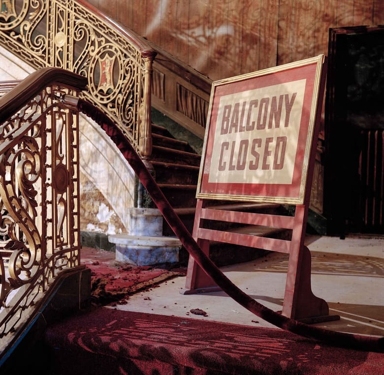 The landing of an old staircase with a sign on it that says "balcony closed"