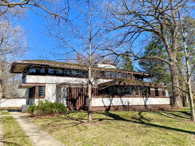 Image of a modern white house with brown trim surrounded by trees without any leaves. 