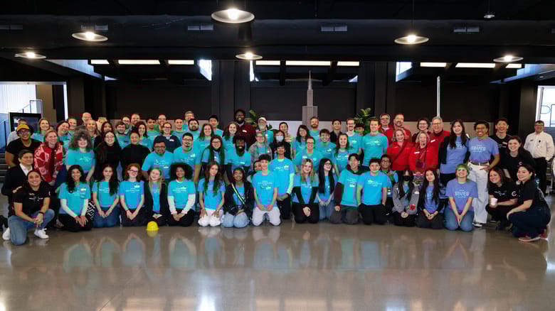 A large group of people in four rows wearing teal, red, or black shorts smiling.