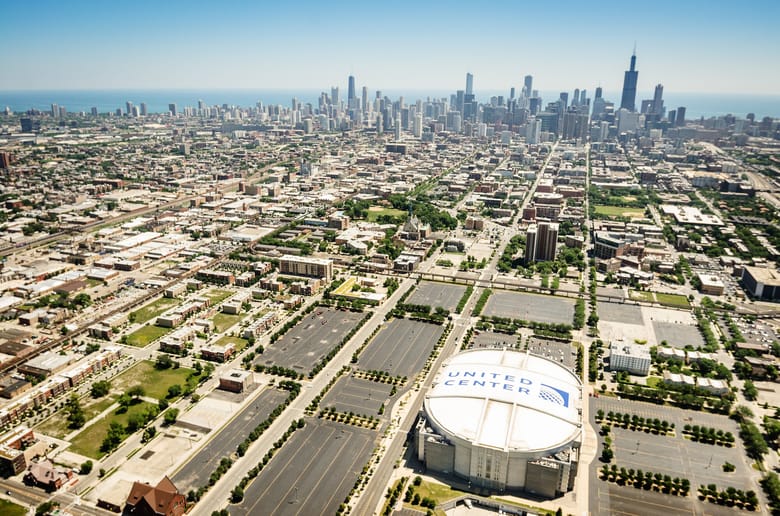 Aerial view of the United Center and surrounding Near West Side neighborhood, with Chicago’s downtown skyline and Lake Michigan visible in the background.