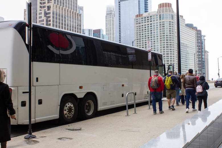 People lining up to board a large white bus. 