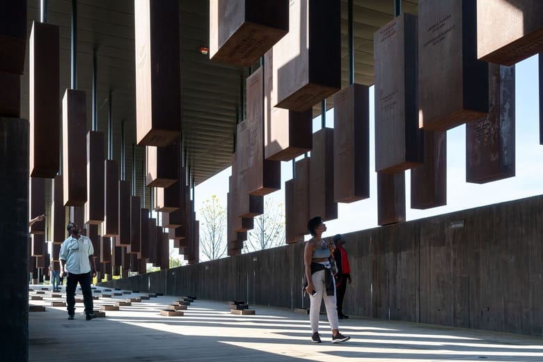 People walking under art sculptures hanging from the ceiling. 