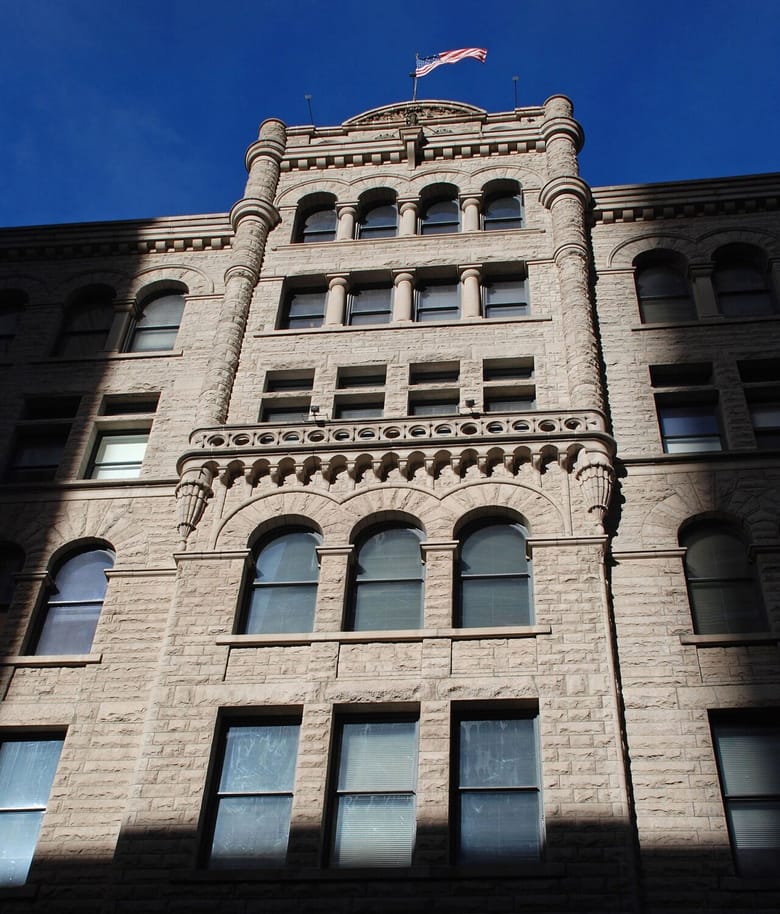 Tan stone building with arched windows and an American flag at the top in the middle. 