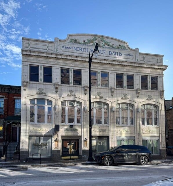 White window lined building with green embellishmnets and a sign with blue text on top that reads "North Avenue Baths"