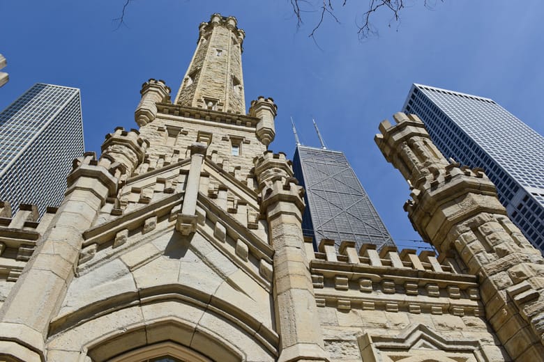 Image looking up at a tall limestone tower with skyscrapers in the background. 